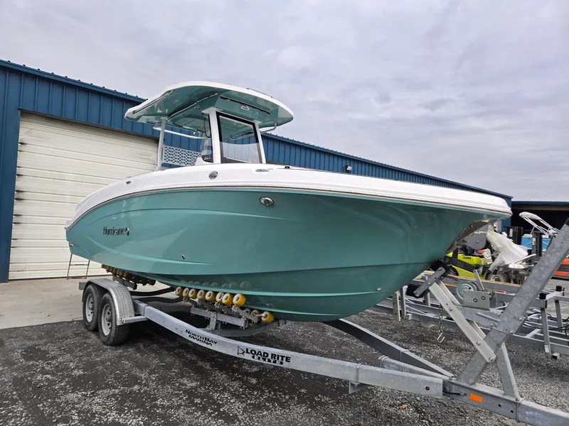 Slide: The Image of 2025 Hurricane Center Console 24 OB boat on trailer, teal hull, parked outside warehouse. - 1
