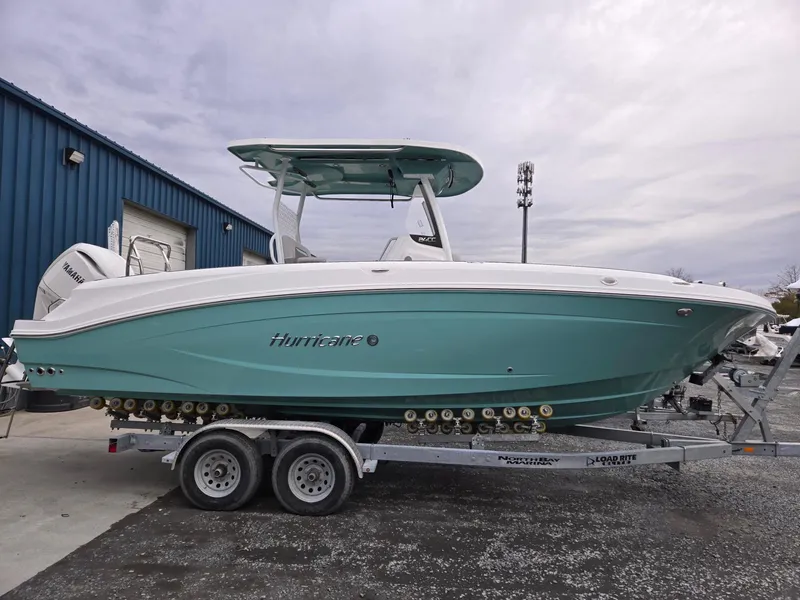 Slide: The Image of 2025 Hurricane Center Console 24 OB boat on trailer, teal hull, parked outdoors. - 2