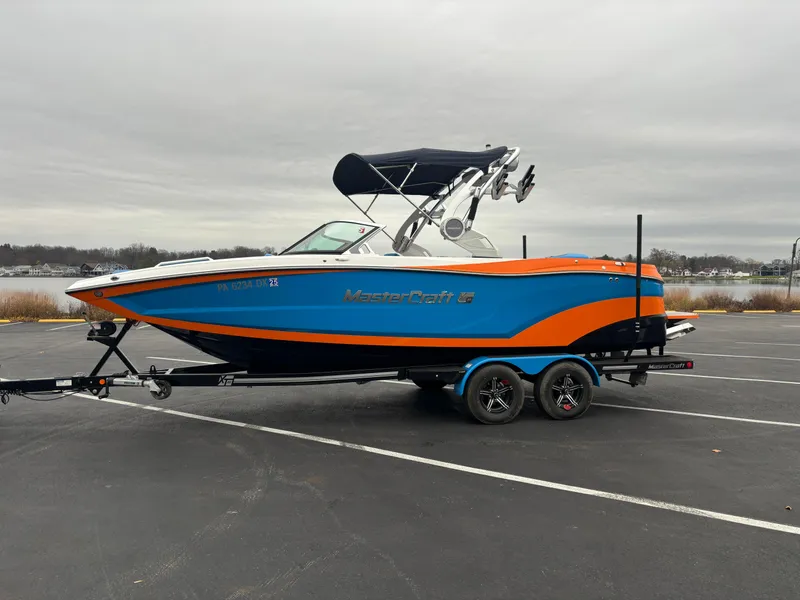 The Image of 2020 MasterCraft XT22 boat with blue and orange design on a trailer. - 0