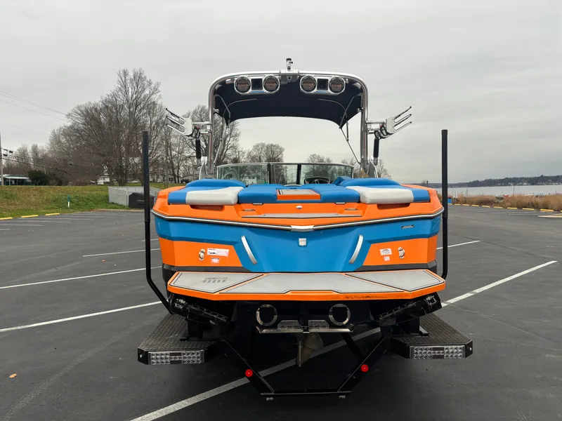 Slide: The Image of 2020 MasterCraft XT22 boat, vibrant orange and blue, parked in a lot near a lake. - 10