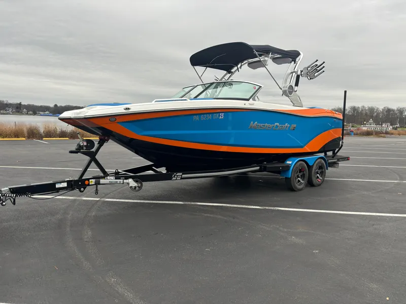 Slide: The Image of 2020 MasterCraft XT22 boat on trailer, vibrant blue and orange design, parked outdoors. - 8
