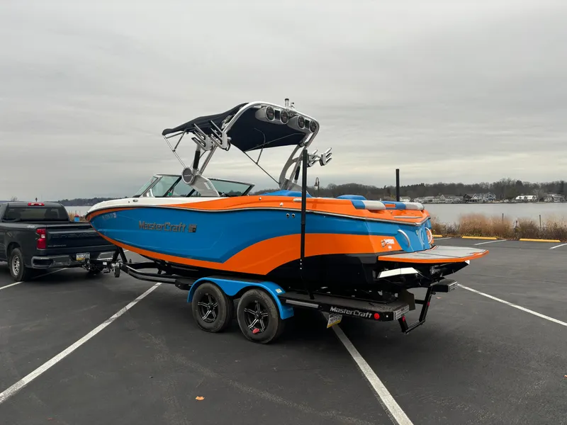 Slide: The Image of 2020 MasterCraft XT22 boat in vibrant orange and blue on a trailer by a lake. - 9