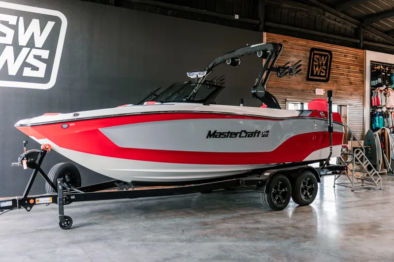 The Image of 2025 MasterCraft XT22 boat in showroom, red and white design on trailer. - 0