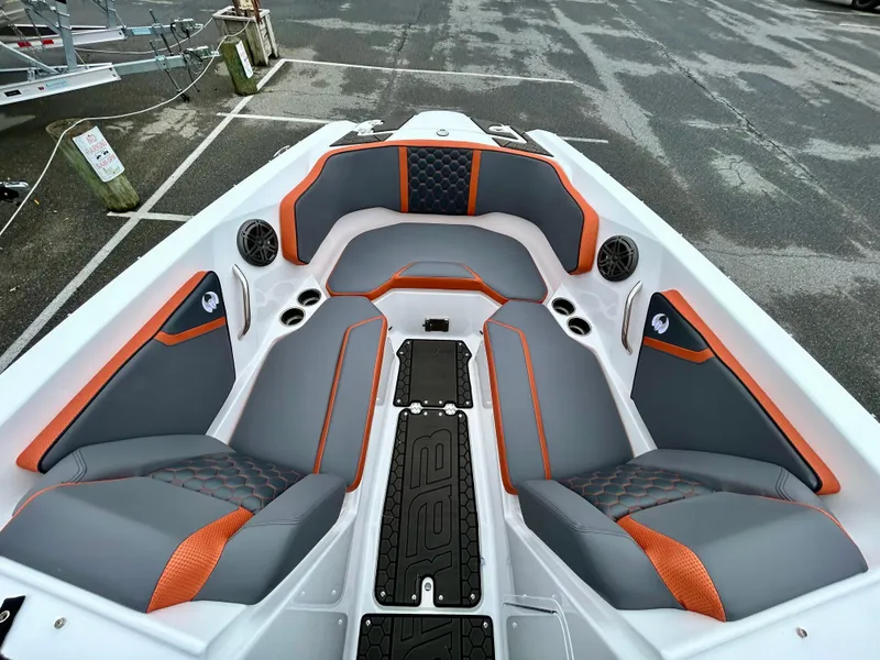 Slide: The Image of 2025 Scarab 255LX boat interior with gray and orange seating, docked in a parking area. - 19