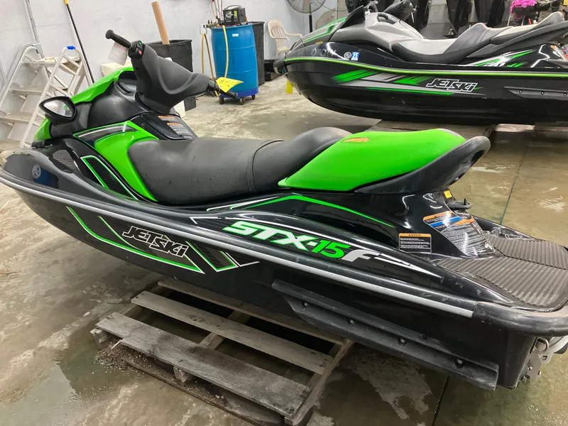 Slide: The Image of 2015 Kawasaki STX15F jet ski in green and black, parked indoors on a pallet. - 2