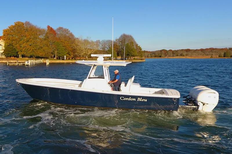 The Image of 2023 Regulator 34 boat cruising on a scenic lake with autumn trees. - 0