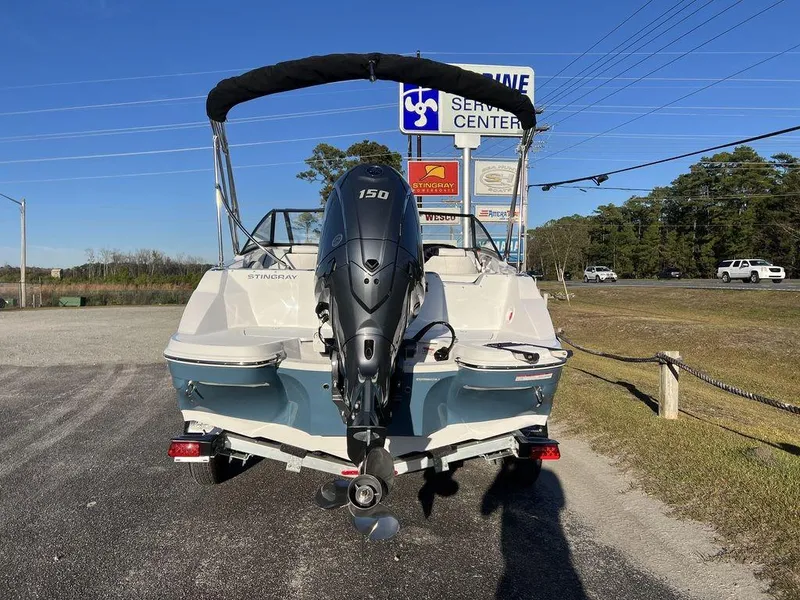 Slide: The Image of 2025 Stingray 201DC boat with outboard motor, parked near a service center under clear blue sky. - 7