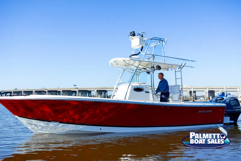 Slide: The Image of 2011 Regulator 28 boat in water, red hull, man steering, Palmetto Boat Sales logo. - 17