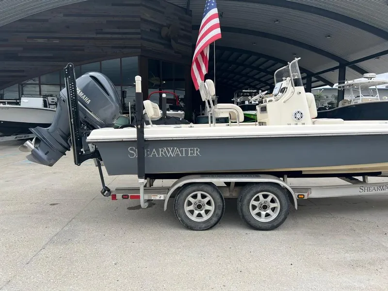 Slide: The Image of 2012 ShearWater 23LTZ boat on trailer with American flag, parked in marina. - 2