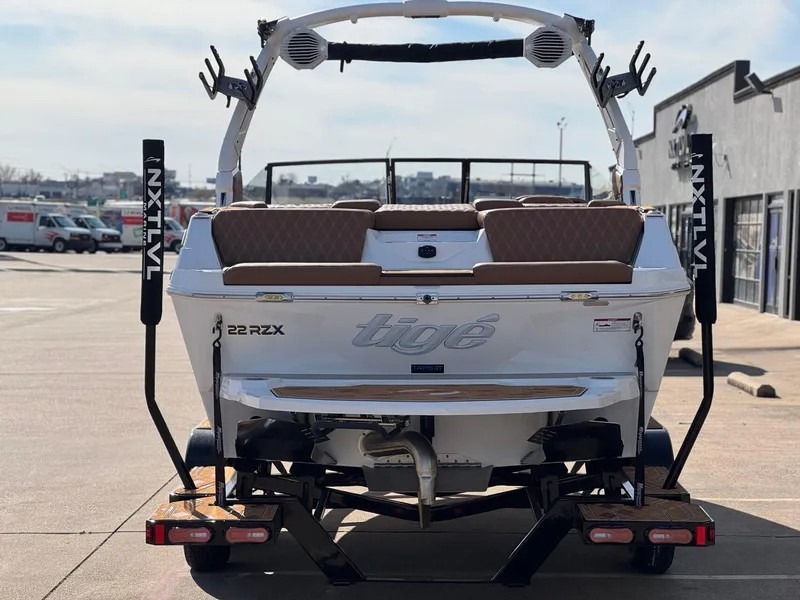 Slide: The Image of 2025 Tigé 22RZX boat rear view, parked on a trailer in a sunny outdoor setting. - 4
