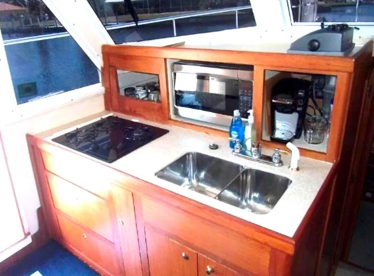 Slide: The Image of Mainship 430 Trawler 2000 kitchen with stove, sink, microwave, and wooden cabinetry. - 16
