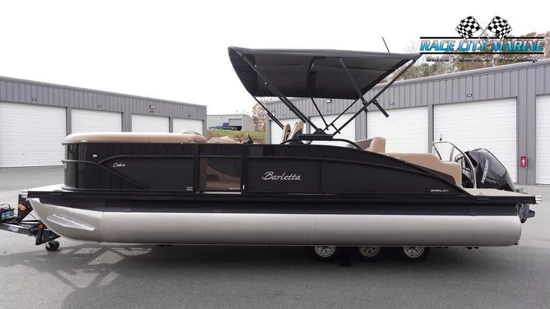 Slide: The Image of 2025 Barletta Cabrio 22UC pontoon boat with canopy, parked outside storage units. - 2