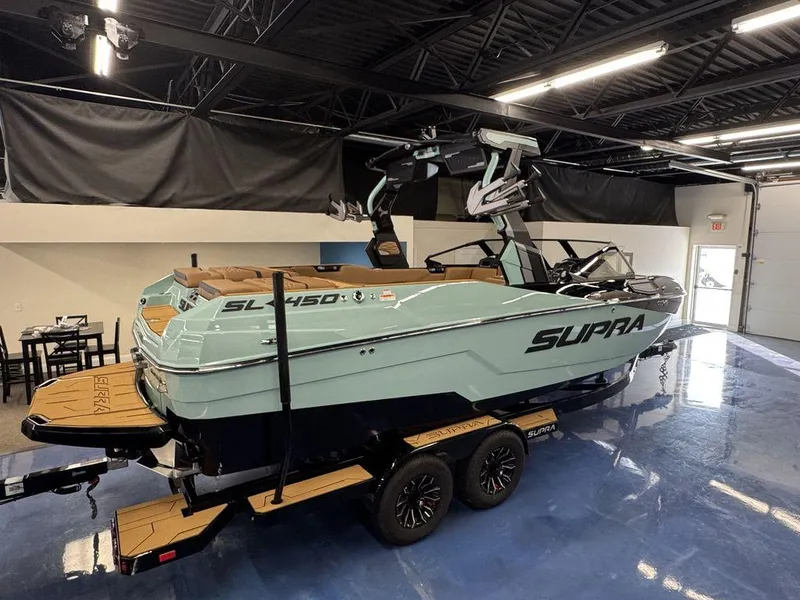 Slide: The Image of 2025 Supra SL 450 boat in showroom, sleek design, mint green color, on trailer. - 6