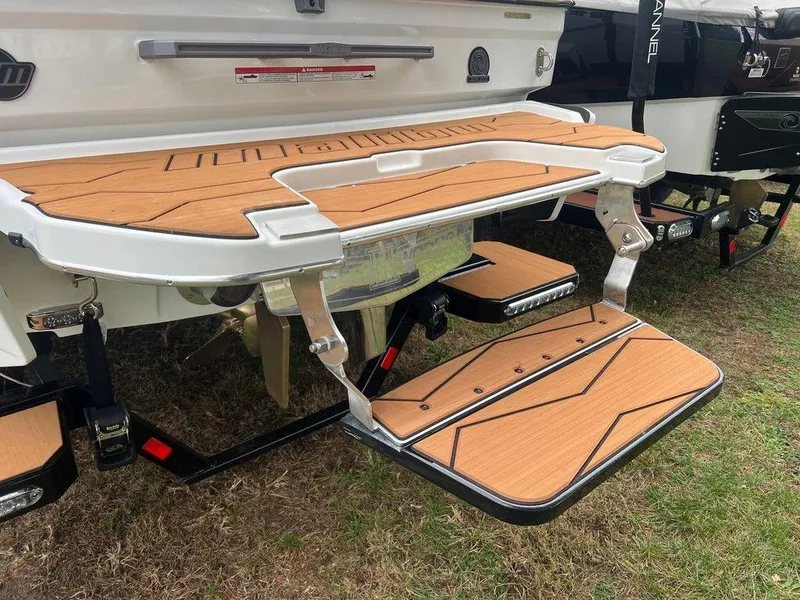 Slide: The Image of 2025 Malibu 23 MXZ boat swim platform with teak finish, displayed on grass. - 21
