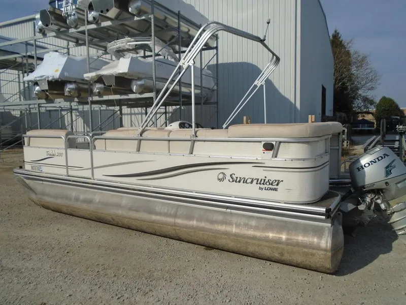 Slide: The Image of 2005 Lowe Trinidad 200 pontoon boat with Honda outboard motor, parked outdoors. - 1