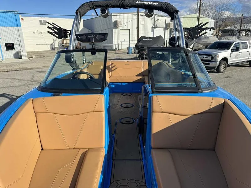 Slide: The Image of 2024 MasterCraft NXT23 boat with tan seats and blue exterior, parked outdoors. - 14