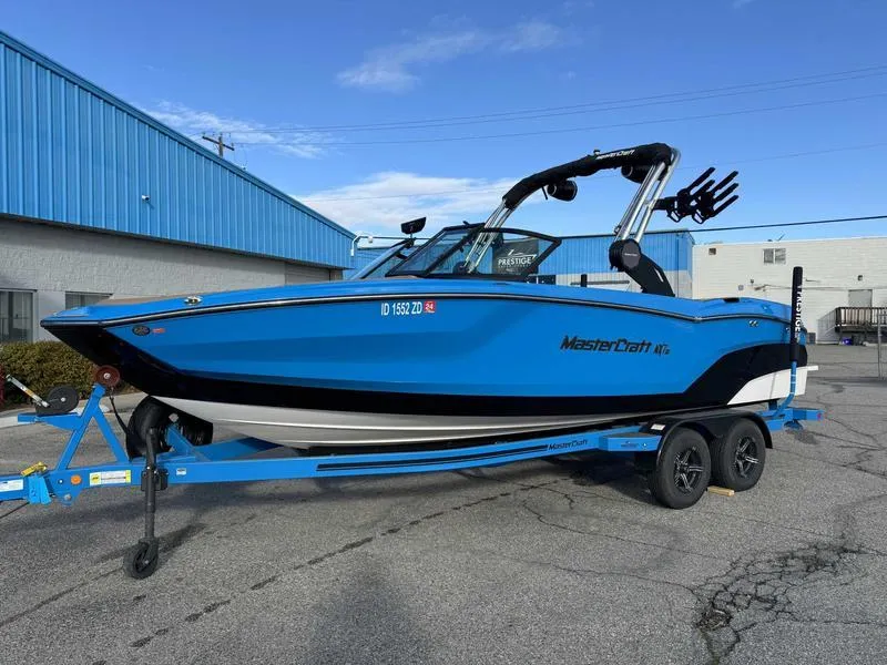 Slide: The Image of 2024 MasterCraft NXT23 boat in vibrant blue on a trailer, parked outdoors. - 3