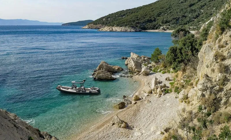 Slide: The Image of Arksen 8 boat in a serene coastal cove, surrounded by rocky cliffs and clear blue water. - 5