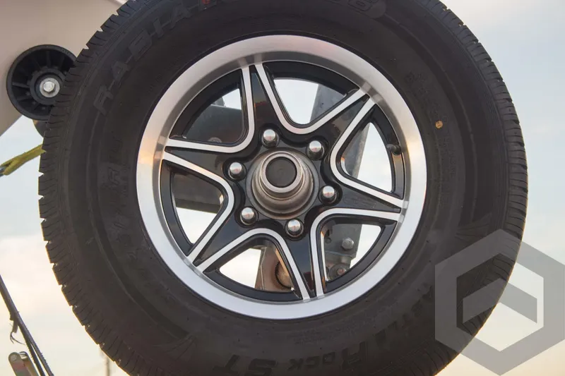 Slide: The Image of Close-up of a 2025 Caymas 26 HB trailer wheel with black and silver rim. - 19