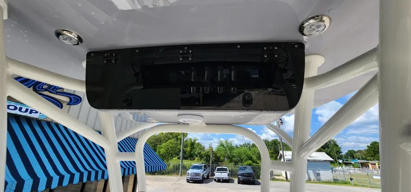 Slide: The Image of 2024 Key West 219fs boat interior with overhead console and blue-striped awning in background. - 32