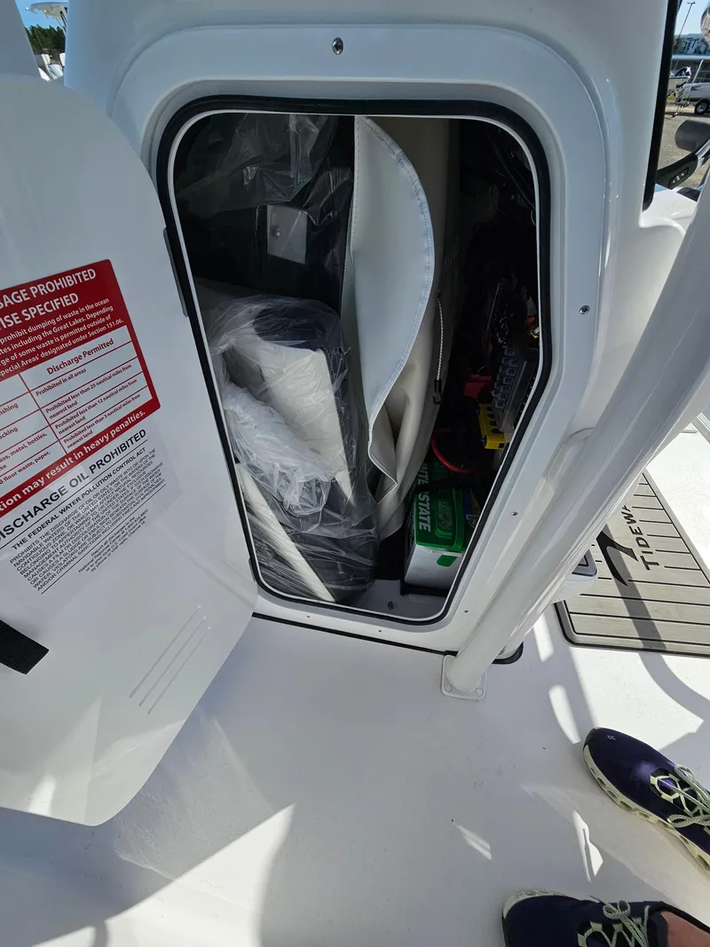 Slide: The Image of Open storage compartment on 2025 Tidewater 220LXF boat, showing interior equipment and safety labels. - 20