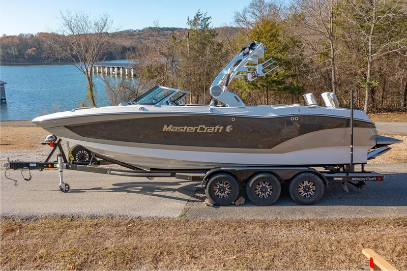 Slide: The Image of 2019 MasterCraft X24 boat on trailer by a lake, surrounded by trees. - 0