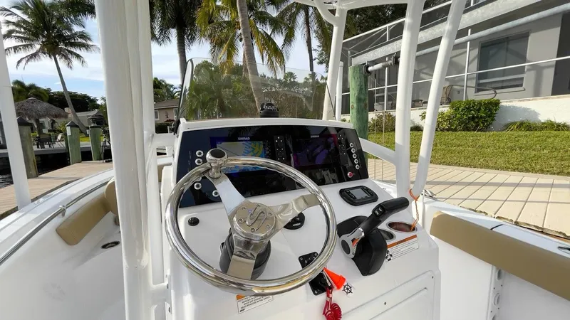 Slide: The Image of 2018 Sportsman Open 212 boat dashboard with steering wheel and controls, docked near palm trees. - 10