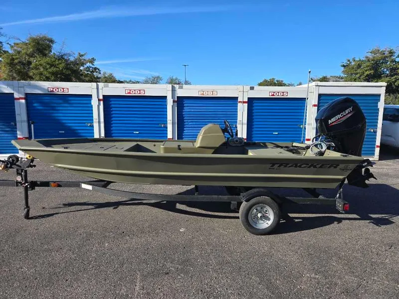 Slide: The Image of 2025 Tracker Grizzly 1648 SC boat on trailer, parked near storage units. - 2