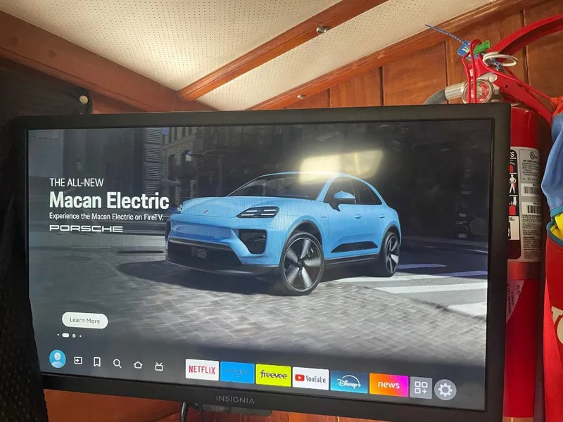 Slide: The Image of TV screen displaying Porsche Macan Electric ad, with streaming apps below, inside a 1979 C & L Explorer Center Cockpit Cutter. - 33