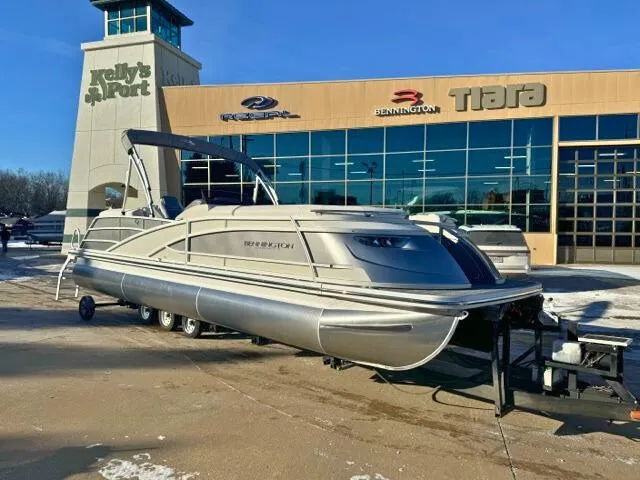 Slide: The Image of 2024 Bennington 25 QFB pontoon boat displayed at dealership, sunny day. - 0