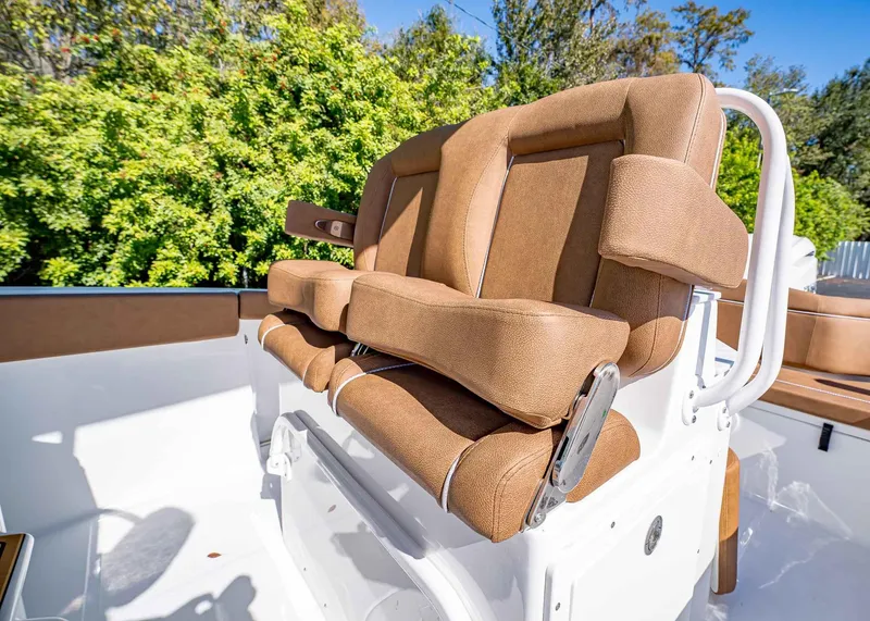 Slide: The Image of 2025 Sea Hunt Ultra 255 SE boat seat with brown upholstery, surrounded by greenery. - 25
