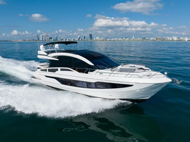 Slide: The Image of 2019 Galeon 650 Sky yacht cruising on open water with city skyline backdrop. - 0