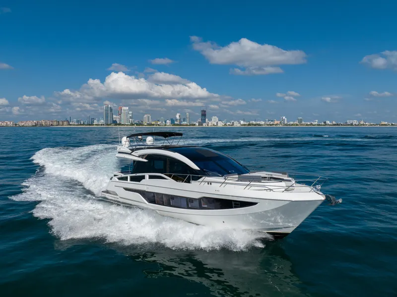 Slide: The Image of 2019 Galeon 650 Sky yacht cruising on open water with city skyline backdrop. - 1