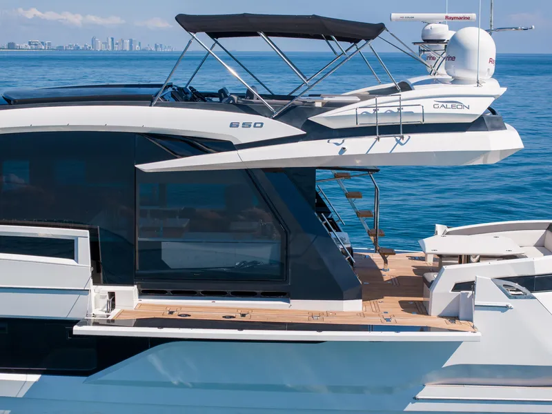 Slide: The Image of 2019 Galeon 650 Sky yacht on calm blue ocean with city skyline in background. - 12