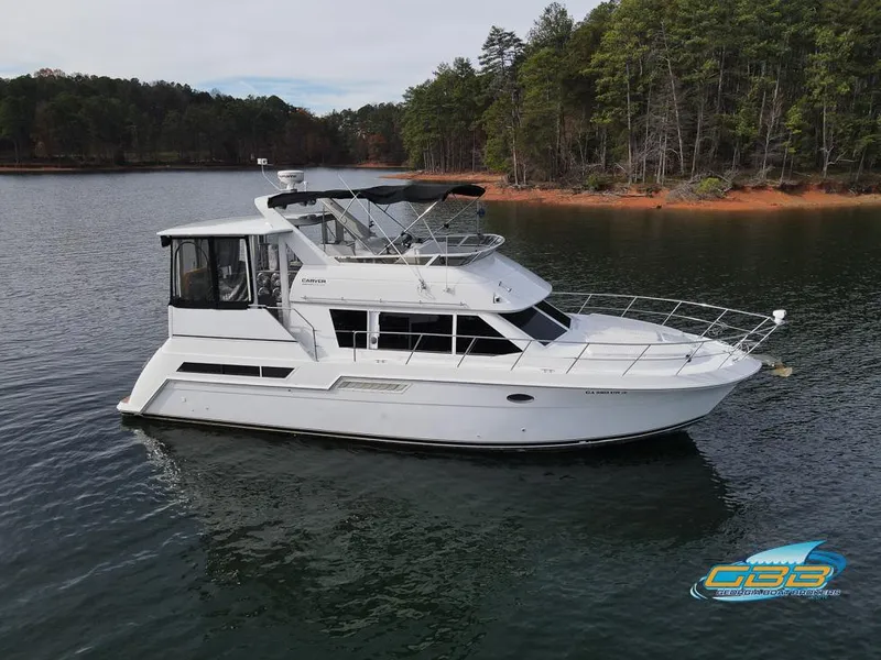The Image of 1998 Carver 405 Aft Cabin yacht on a serene lake with forested shoreline. - 1