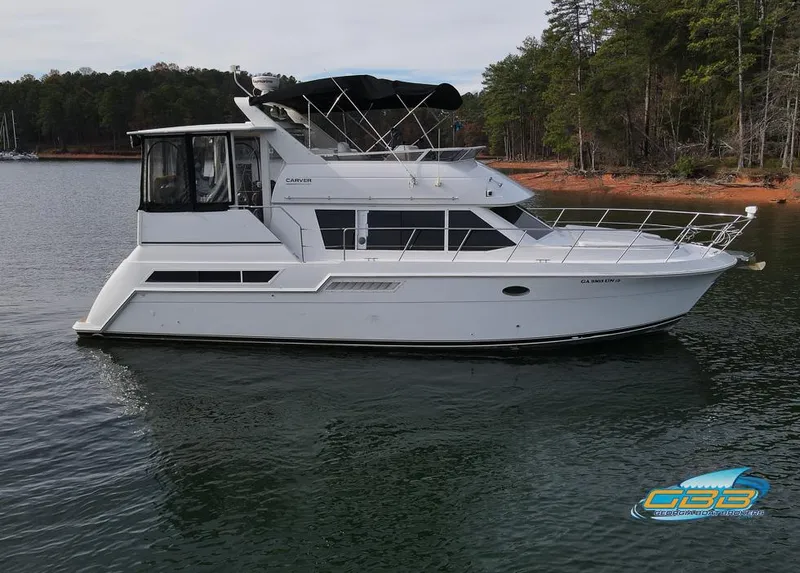 Slide: The Image of 1998 Carver 405 Aft Cabin yacht on a serene lake with forested shoreline. - 6