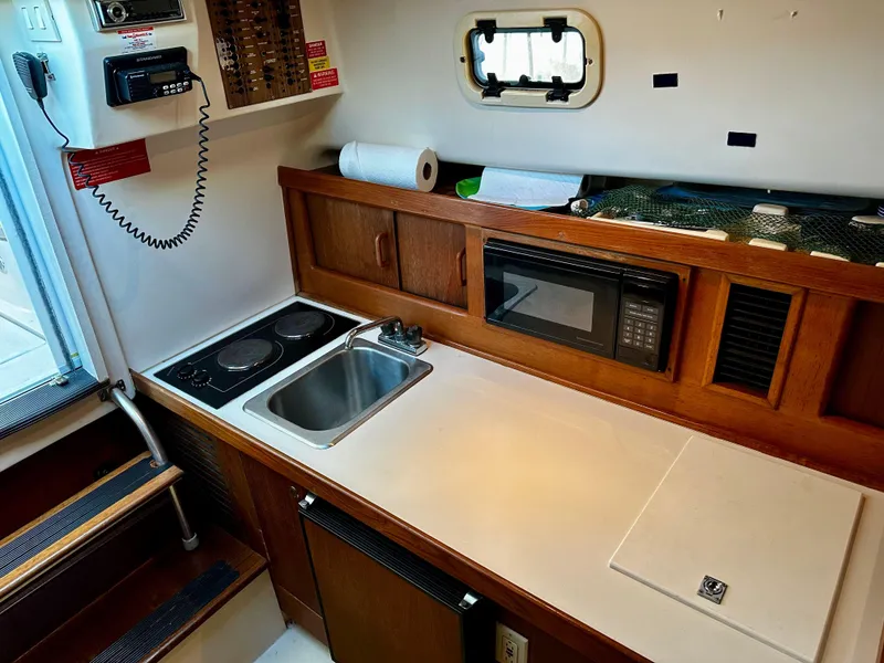 Slide: The Image of 2000 Mainship Pilot 30 Sedan galley with stove, sink, microwave, and compact fridge. - 17