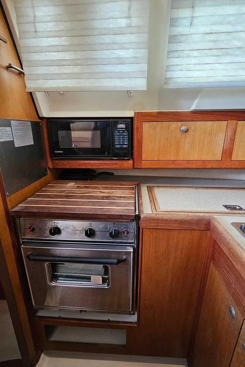 Slide: The Image of 1998 Hunter 340 Sloop kitchen with stove, microwave, and wooden cabinetry. - 13