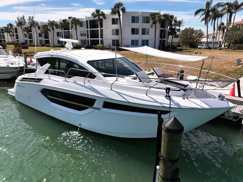 The Image of 2019 Cruisers Yachts 42 Cantius docked near waterfront apartments, surrounded by palm trees. - 0