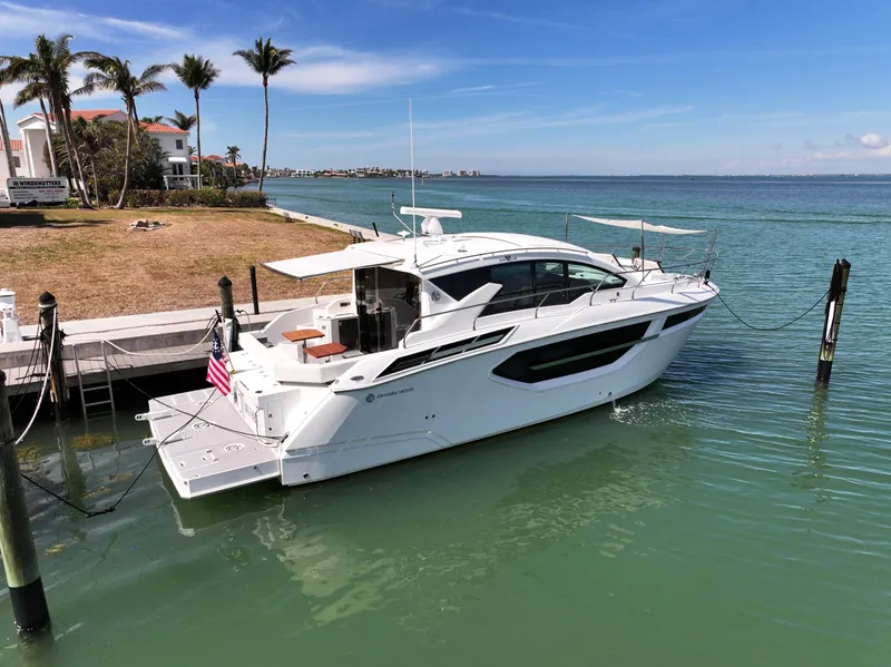 Slide: The Image of 2019 Cruisers Yachts 42 Cantius docked by a scenic waterfront with palm trees. - 2