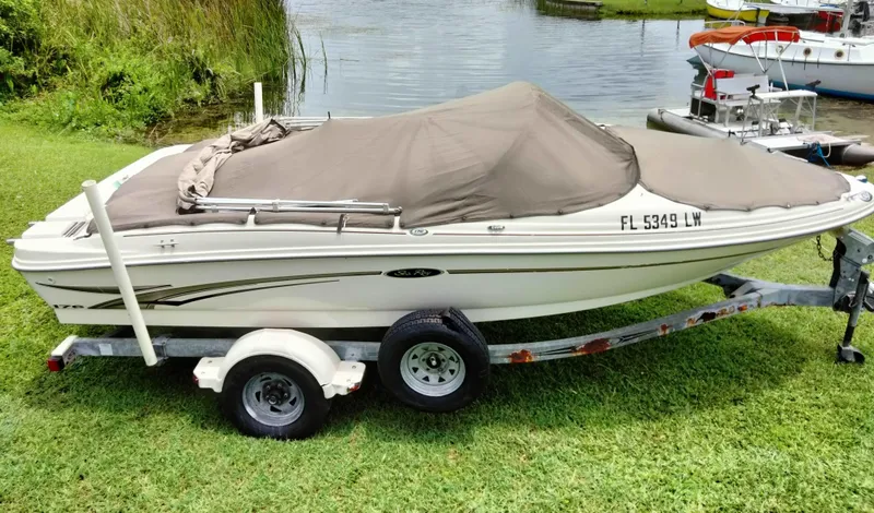 Slide: The Image of 2002 Sea Ray 176 Bow Rider boat on trailer, covered, near a lake. - 18