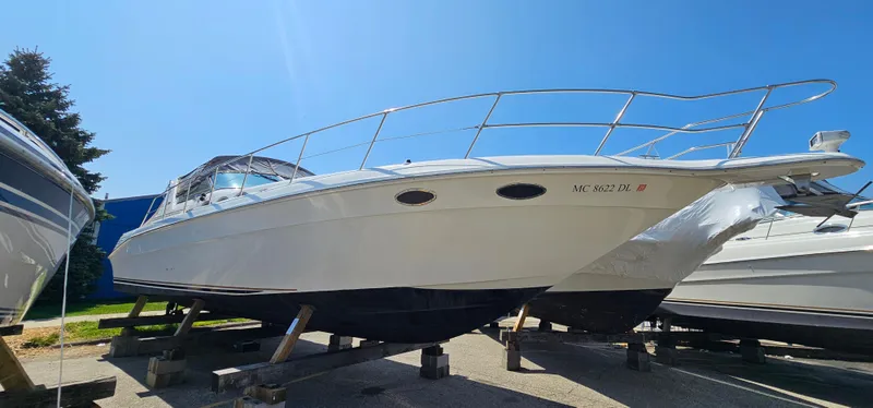 The Image of 1999 Sea Ray 400 Express Cruiser on dry dock, flanked by other boats, under clear blue sky. - 0