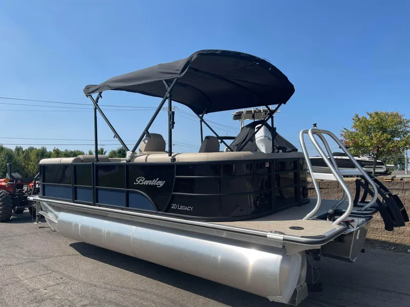 Slide: The Image of 2024 Bentley Pontoons Legacy 200 Navigator, black pontoon boat with canopy, parked outdoors. - 2
