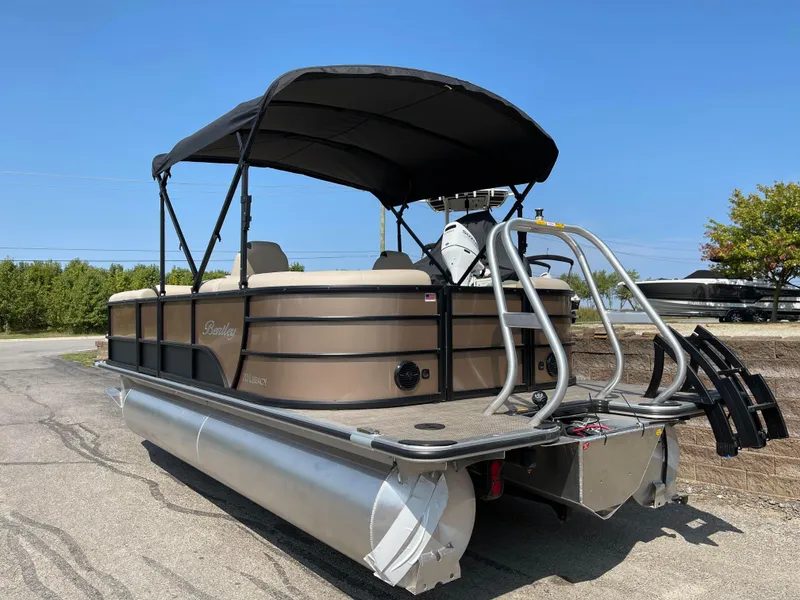Slide: The Image of 2024 Bentley Pontoons Legacy 200 Navigator with canopy, parked on pavement under clear blue sky. - 2