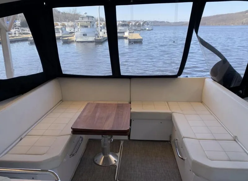 Slide: The Image of 2018 Cruisers 390 Express Coupe interior with white seating and wooden table, overlooking marina. - 10