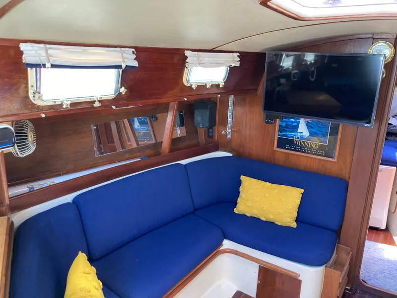 Slide: The Image of Interior of 1984 Irwin 34 Sloop with blue seating, yellow pillows, and mounted TV. - 3