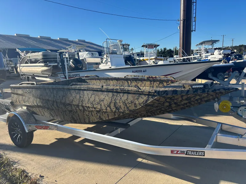 The Image of 2025 Edge Duck Boats 556 DB on trailer, camo design, parked at marina. - 1