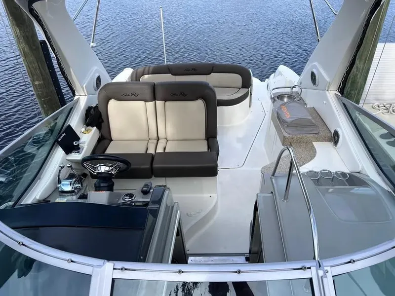 Slide: The Image of 2015 Sea Ray 330 Sundancer boat interior with seating and helm, docked on calm water. - 11