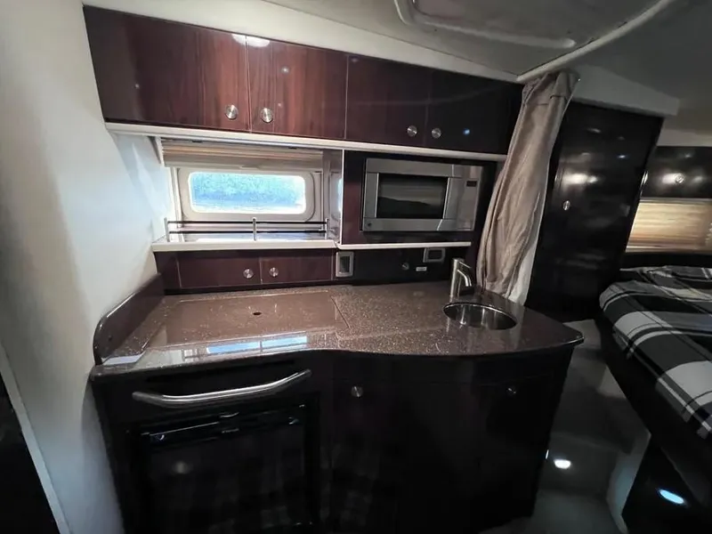 Slide: The Image of 2015 Sea Ray 330 Sundancer interior kitchen with dark wood cabinets and modern appliances. - 17