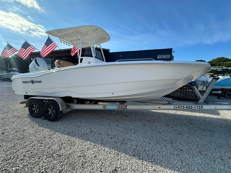 Slide: The Image of 2025 NauticStar 231 Hybrid boat on trailer with American flags in background. - 2